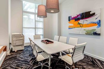 A conference room with a white table and chairs, a large abstract painting on the wall, and a floor lamp.